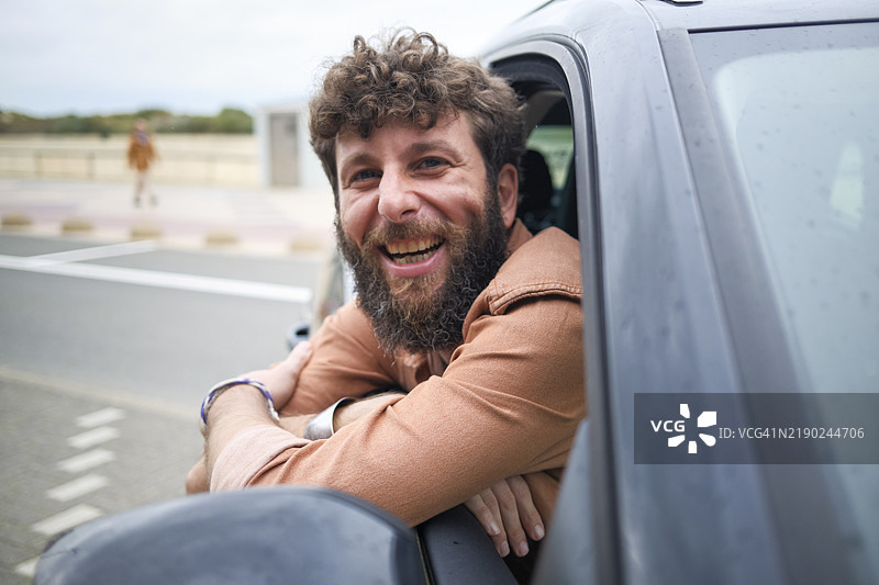 微笑的胡子男人靠在车窗外，散发出愉快和放松的气息图片素材