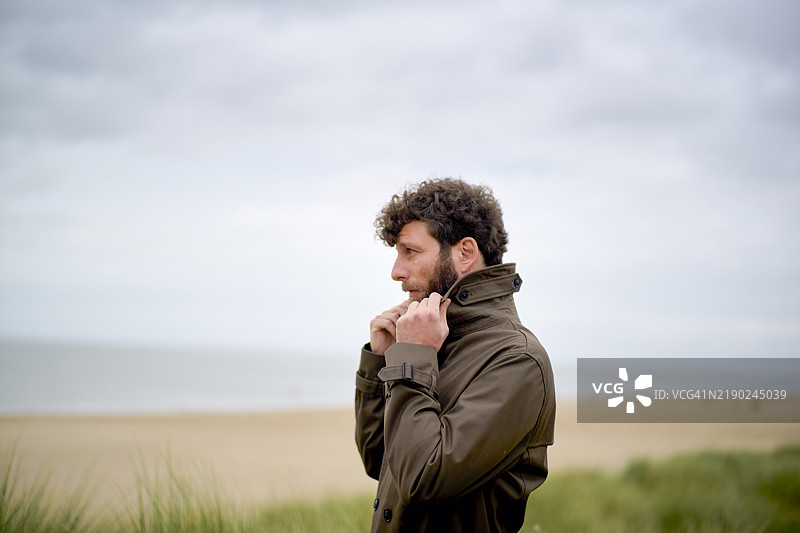 穿着夹克的男子在比利时的海滩上思考，寒冷的天气和阴云密布的天空。图片素材