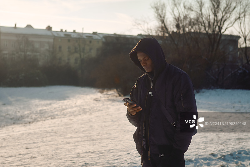 年轻男子在德国柏林的日落时分站在雪中看手机图片素材