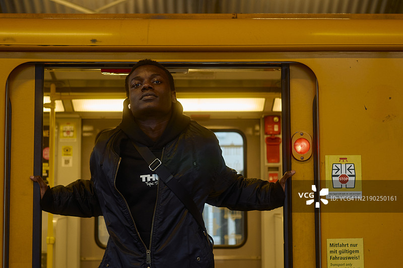 年轻男子自信而充满活力地站在火车的开门之间，德国柏林图片素材