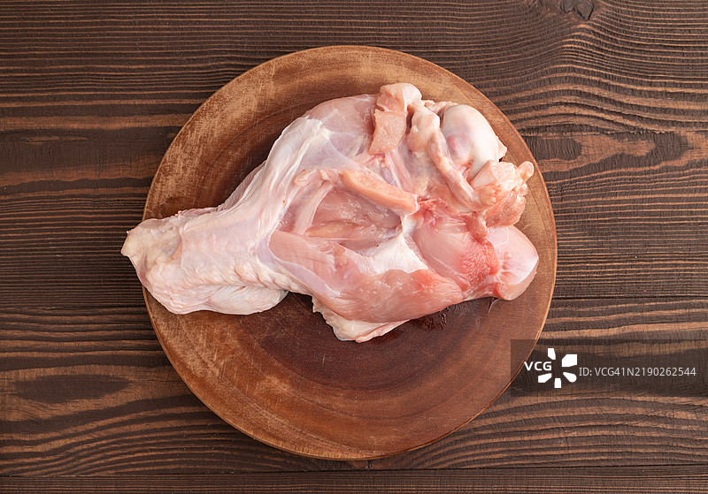 生火鸡翅在木质砧板上，背景为棕色木纹。俯视图，特写。图片素材