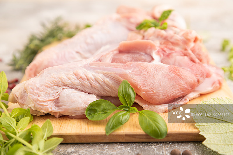 带香草和香料的生火鸡翅在木质切菜板上，背景为棕色混凝土。侧面视图，特写，选择性对焦。图片素材