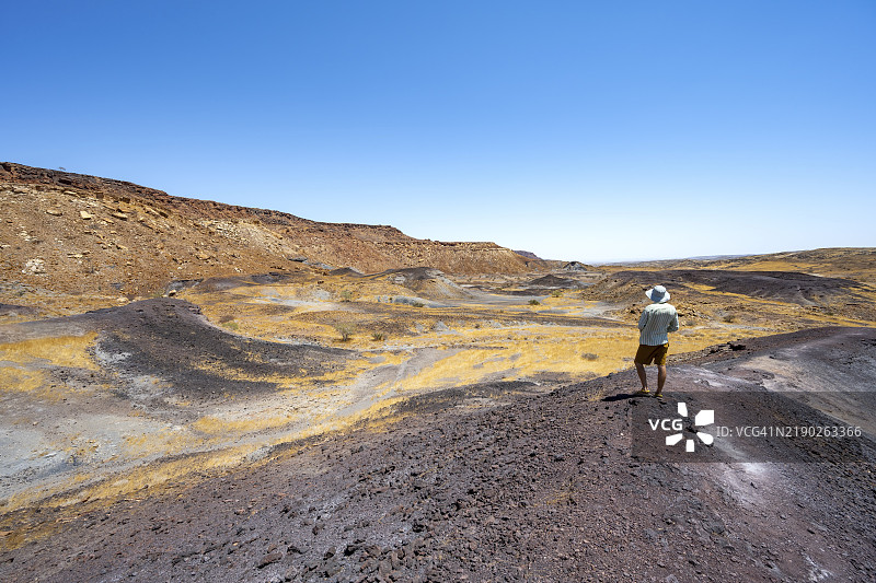 游客在山丘上欣赏风景，干燥的黄草地和黑色火山丘，烧焦的山，达马拉兰，库内内，纳米比亚，非洲图片素材