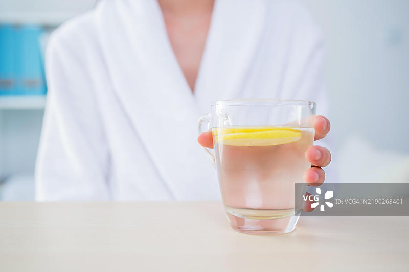 穿着白色浴袍的女人手里拿着一杯加柠檬的水图片素材