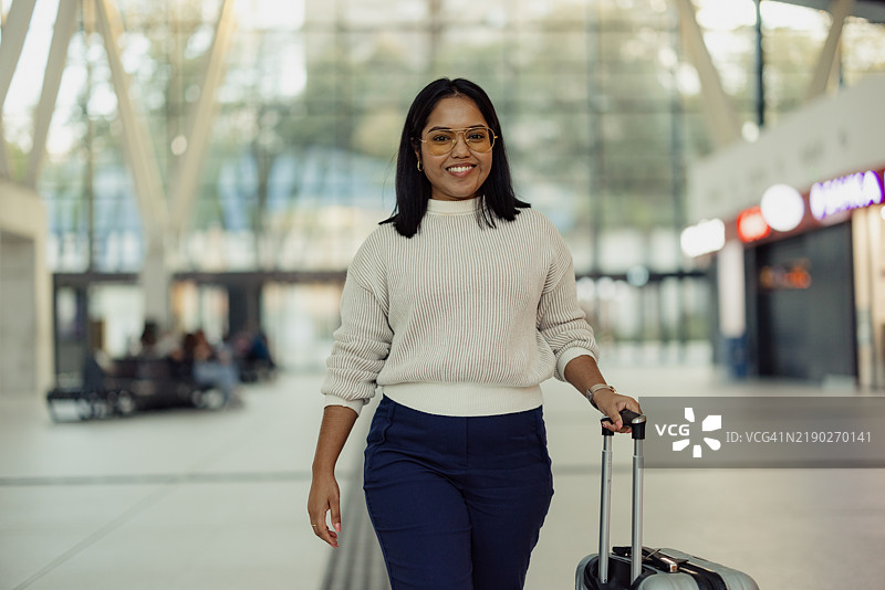 自信的女性旅行者在现代机场航站楼中拖着行李走过图片素材