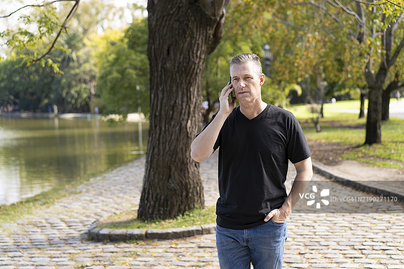 一位五十多岁的男子在湖边走路时打电话图片素材