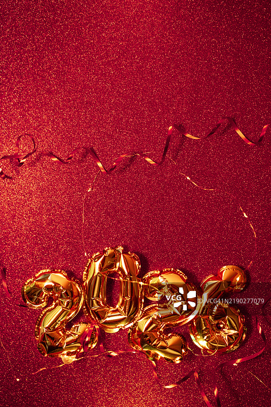 金色气球呈现出2026的形状，映衬在明亮的红色背景上，搭配闪闪发光的节日丝带，营造出欢乐和庆祝的新年氛围。图片素材