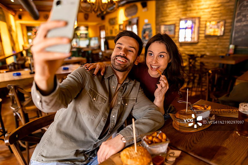 快乐的情侣在餐厅里吃汉堡时自拍图片素材