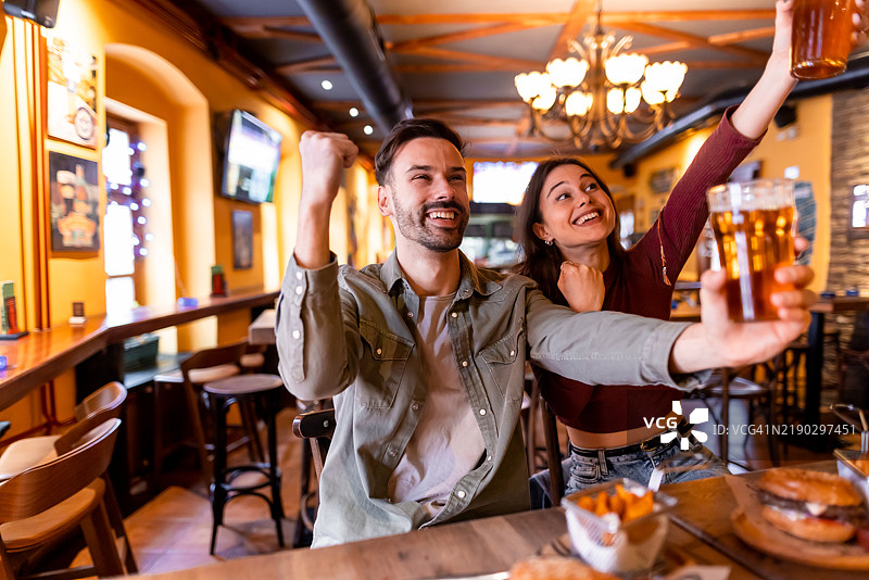 兴奋的情侣在酒吧欢呼并举杯畅饮啤酒图片素材