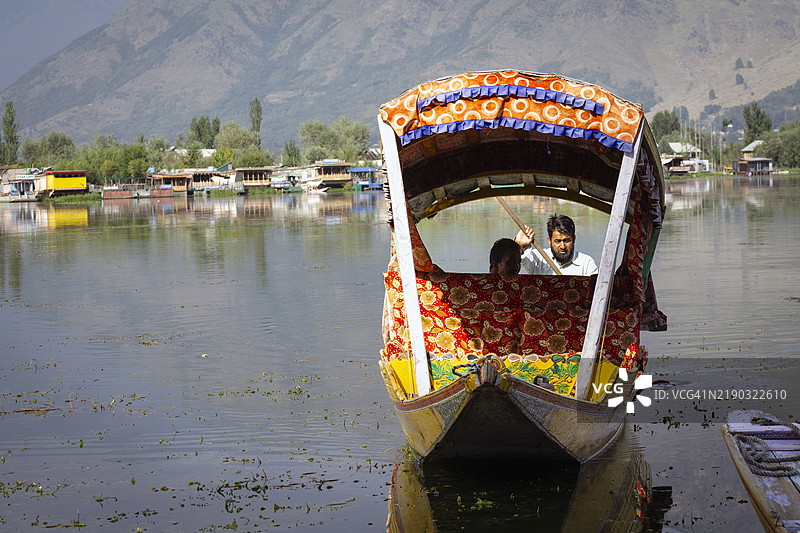在达尔湖平静的水面上，一名男子划着他的什卡拉船，经过迷人的房船，展现了传统与美丽在这个位于克什米尔心脏地带的宁静天堂中的融合。图片素材
