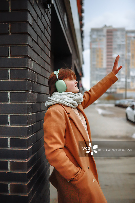 冬季氛围：穿着米色外套和围巾的少女戴着大耳机听音乐。图片素材