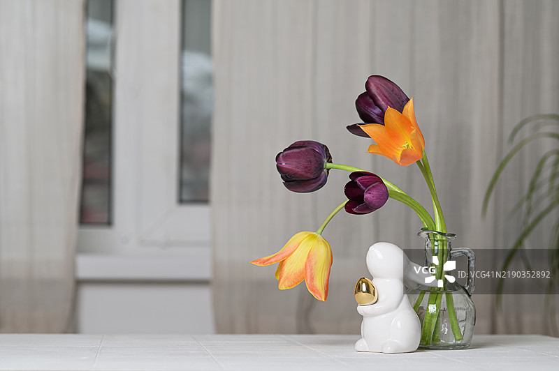 桌子上装有陶瓷兔子装饰的玻璃花瓶中的鲜艳郁金香图片素材