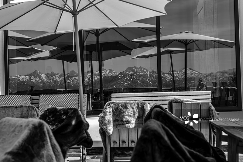 窗户反射和一位坐在餐厅露台上的女性，背景是安德马特的山景和晴朗的夏日天空图片素材