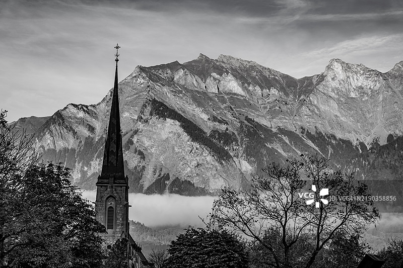 美丽的秋季森林、教堂塔楼、山脉和阳光明媚的天空，阳光洒在巴德拉加兹的晴朗日子里。图片素材