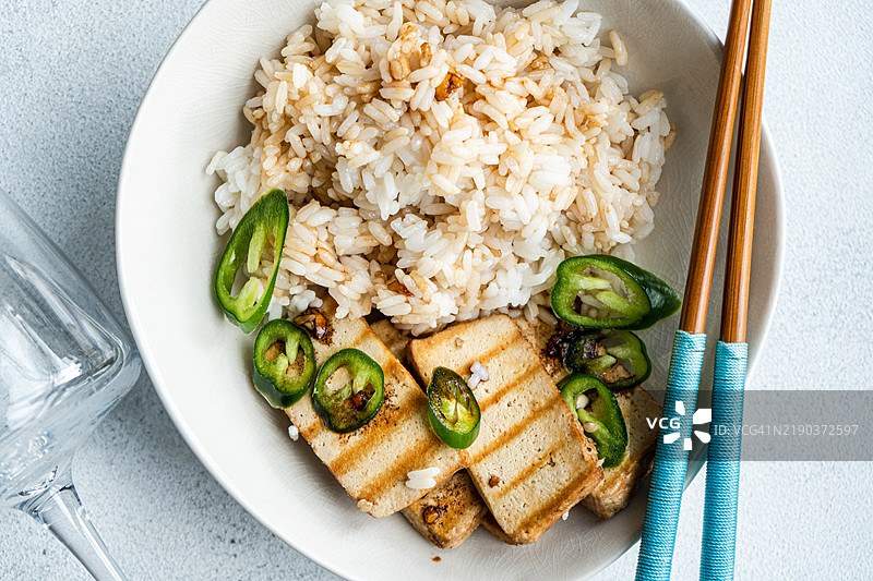 从上方俯视一碗米饭，上面放有切片的烧烤豆腐奶酪、新鲜辣椒和酱油。图片素材