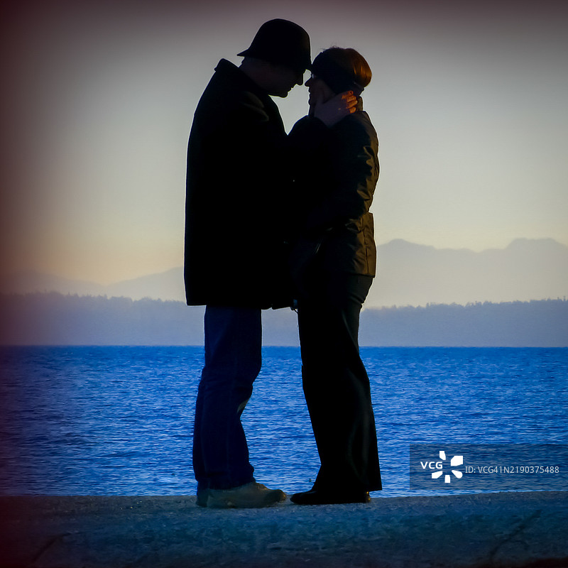 一对老年夫妇在海边面对面站立，背后是维多利亚（加拿大不列颠哥伦比亚省）的山脉轮廓。图片素材