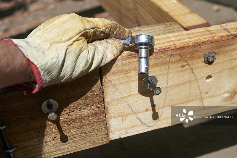 建筑工人在木梁上用棘轮扳手拧紧螺栓图片素材