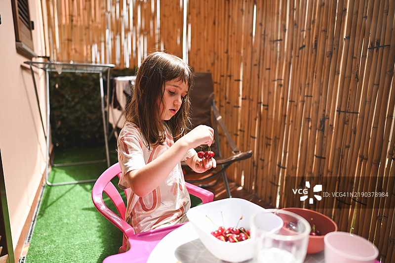 小女孩在院子里吃樱桃。图片素材