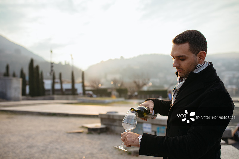 男人在风景如画的户外日落时分倒红酒图片素材