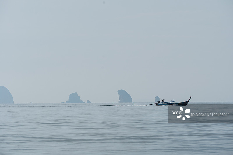 在泰国的石灰岩悬崖附近，长尾船在平静的水域中航行。图片素材