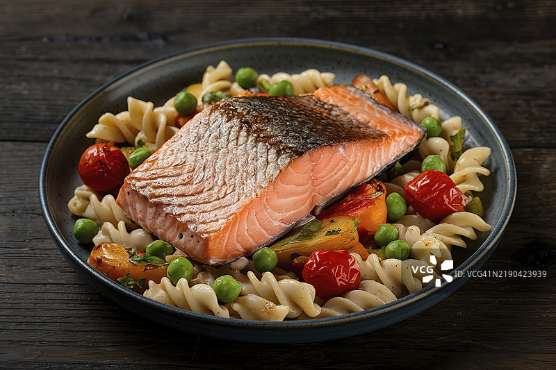 一块煎制的三文鱼片特写，搭配蔬菜和意大利面的盘子。图片素材
