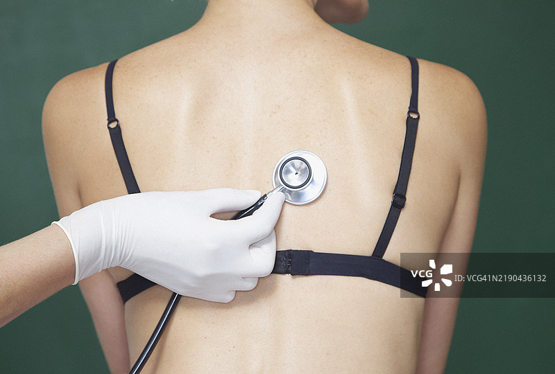 医生的手将听诊器放在女性的背部图片素材