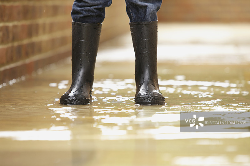 男孩穿着威尔士靴的腿在被淹没的人行道上图片素材