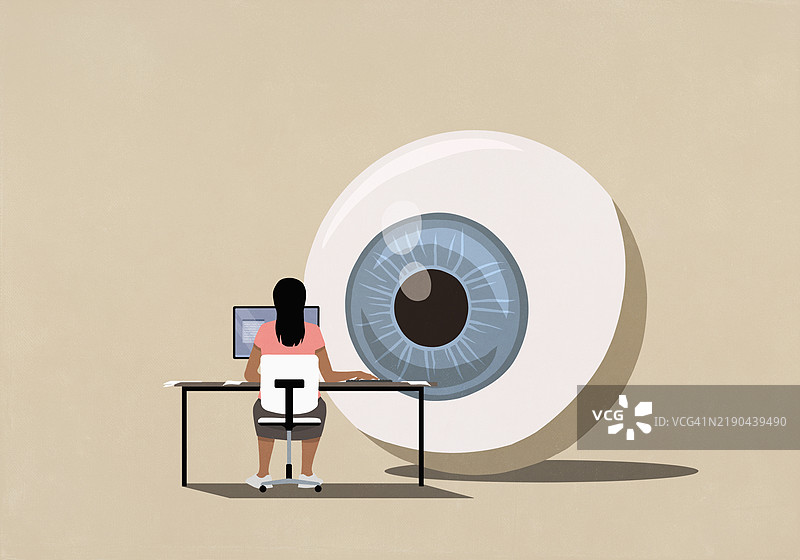 大型监控眼球注视着在桌子上使用电脑的女性图片素材