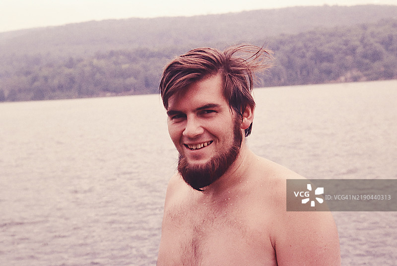 夏季湖边微笑的年轻棕发男子肖像，留着胡须图片素材