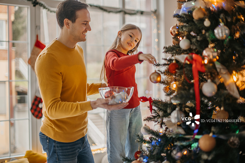 父亲和女儿在节日期间装饰圣诞树图片素材