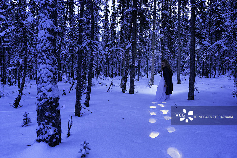 女人在雪-covered森林中行走，留下发光的足迹图片素材