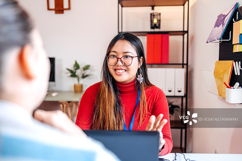 年轻女性在保险公司办公室与客户进行轻松对话，提供建议。图片素材