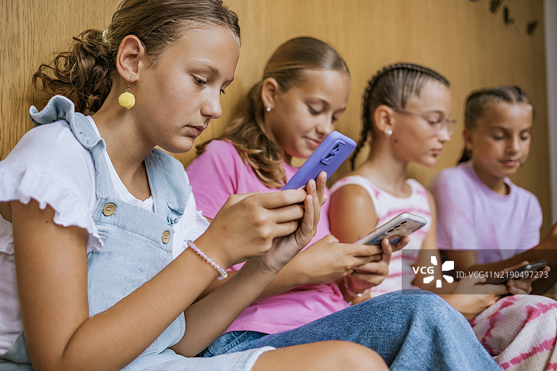学生们在学校的休息时间使用手机，专注于他们的设备，享受轻松的环境。图片素材