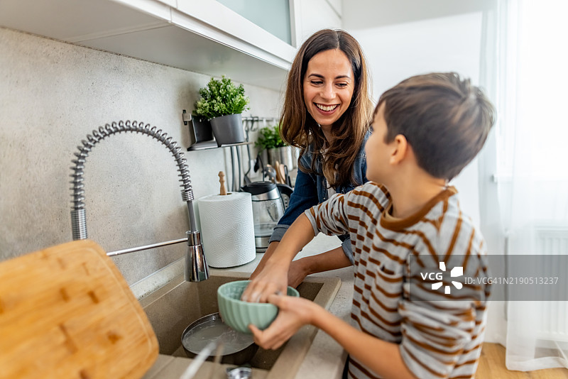 微笑的妈妈和孩子并肩清洗厨房碗碟，分享愉快的家庭时光图片素材