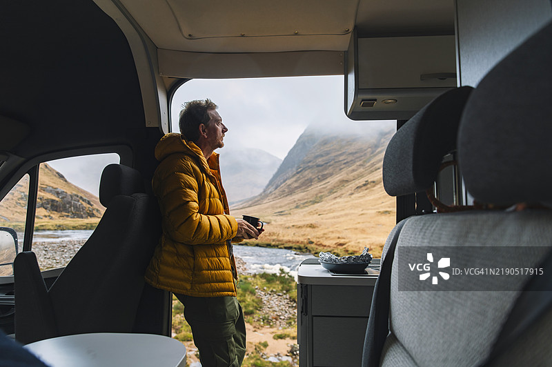 一位成熟的男子在湿润的冬日里，从他的房车中欣赏苏格兰高地的美景。图片素材