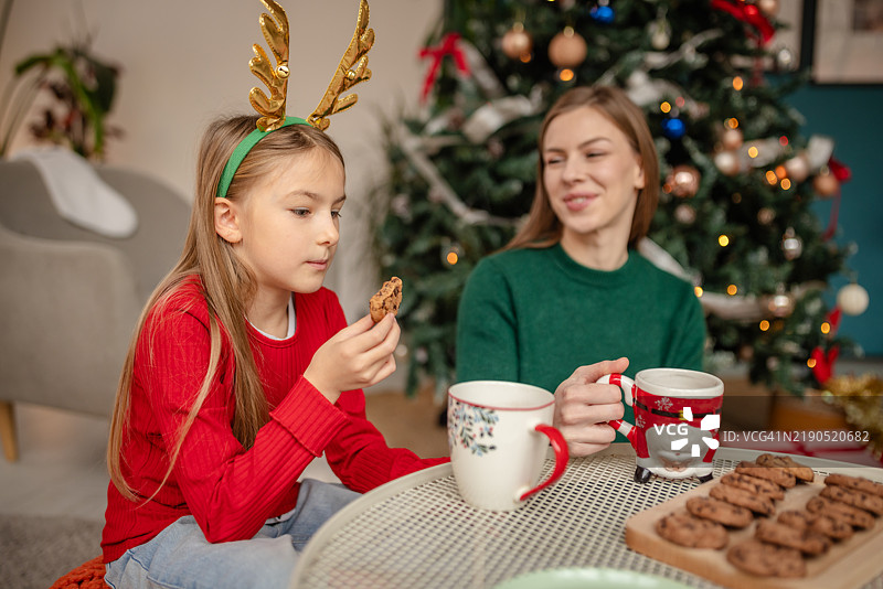 母女俩在装饰华丽的圣诞树旁享用圣诞饼干图片素材