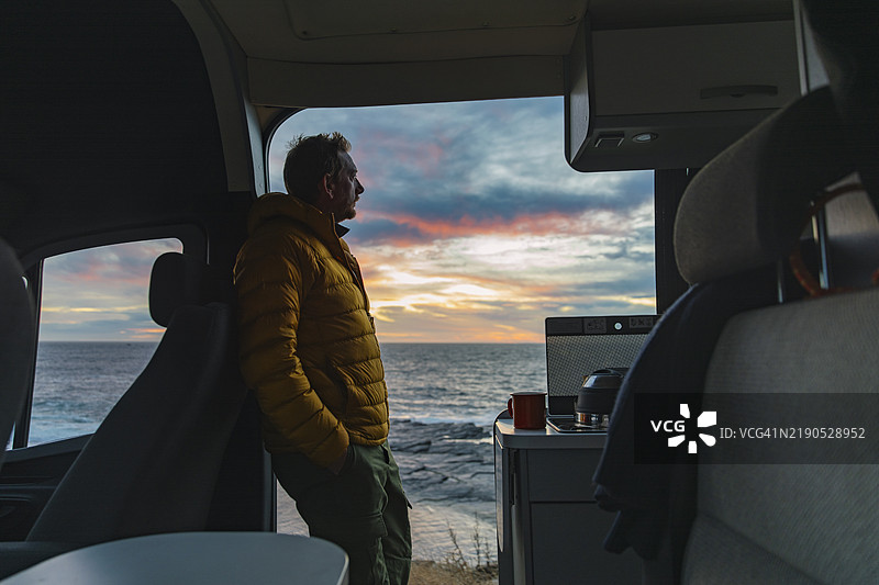 一位成熟的男士在冬季的早晨，从他的房车中欣赏海景——他在等待日出穿透北海的云层。图片素材