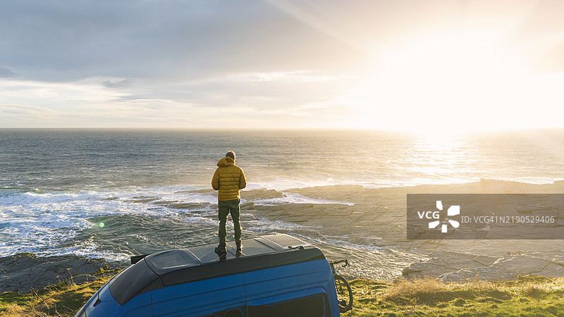 一位成熟的男子站在他的房车顶上，迎接北海的日出。图片素材