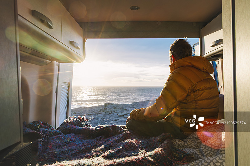 一个男人背对着美丽的海上日出，欣赏冬日清晨的日出景色。图片素材