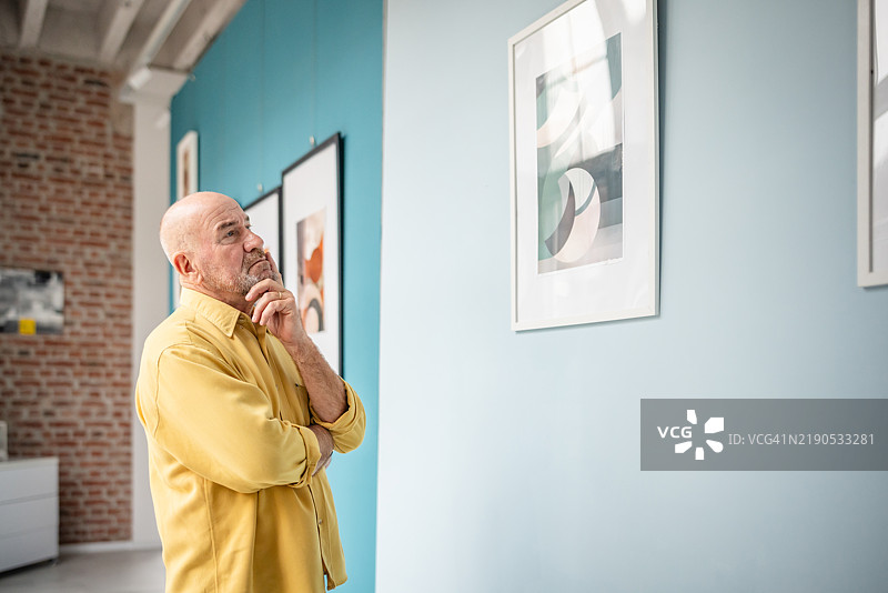 男子在色彩斑斓的现代画廊中观察装裱的抽象艺术作品图片素材