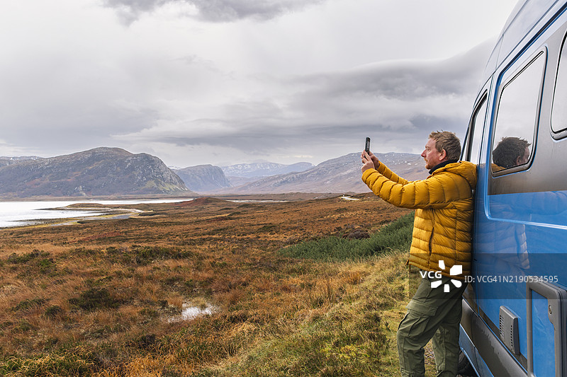 一位成熟的男士在阴云密布的冬日，从他的房车内拍摄洛赫埃里博尔和山脉的景色。图片素材