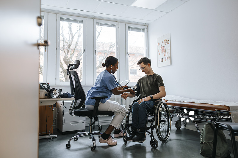 女医生在诊所的检查室里为坐在轮椅上的少年测量血压图片素材