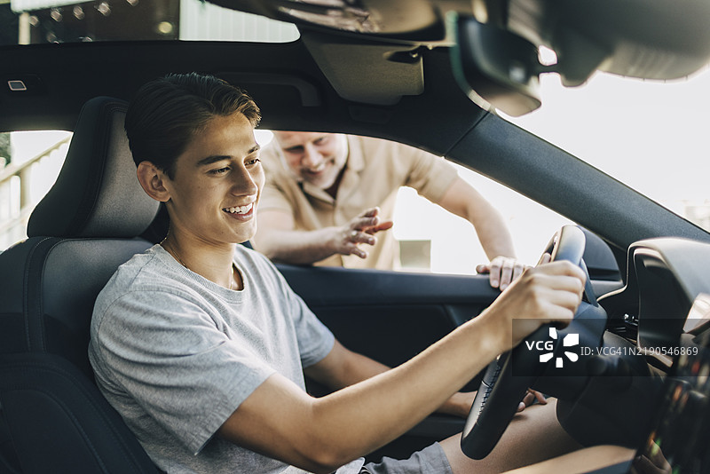 父亲在开车时帮助坐着的儿子图片素材