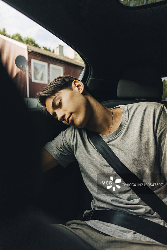 疲惫的年轻男子在公路旅行中坐着打盹，系着安全带。图片素材