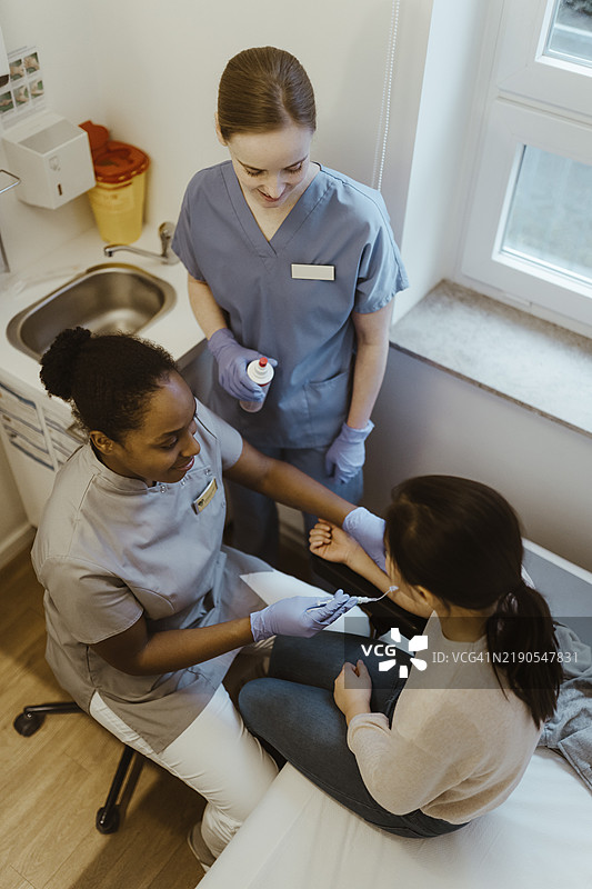 从高处俯视女医学专家在诊所为坐着的女孩采集血样图片素材