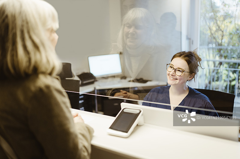 微笑的女性医务工作者在医院接待处协助老年患者图片素材