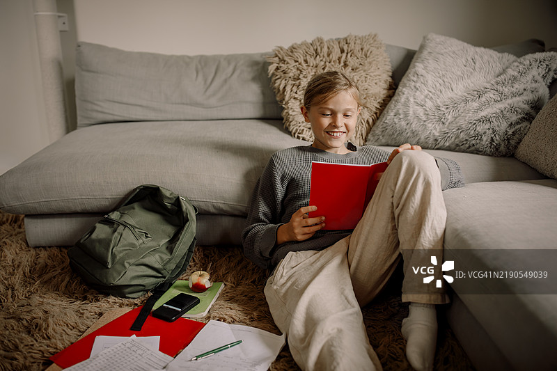 微笑的男孩坐在家里的沙发旁学习图片素材