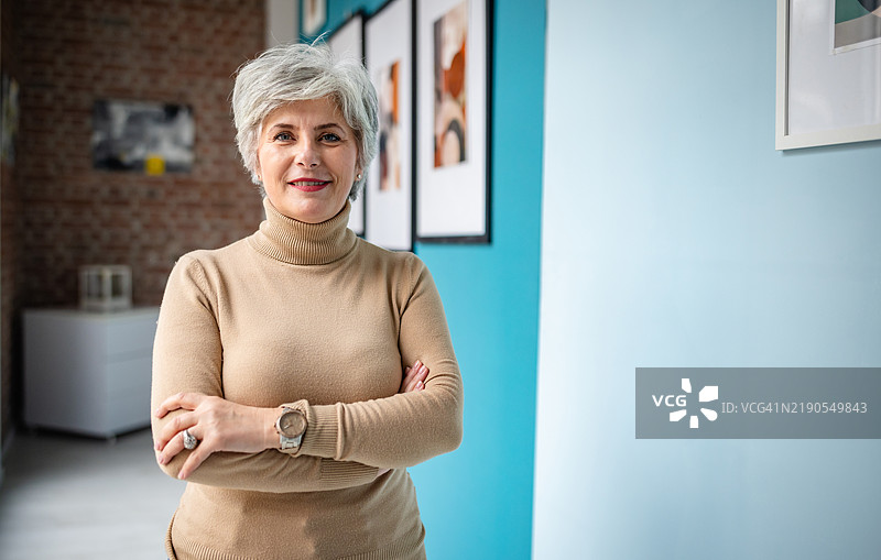 自信的成熟的女性在优雅的室内环境中微笑，周围挂着装裱的艺术作品。图片素材