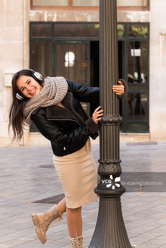 年轻女性在城市中戴着耳机和围巾跳舞图片素材
