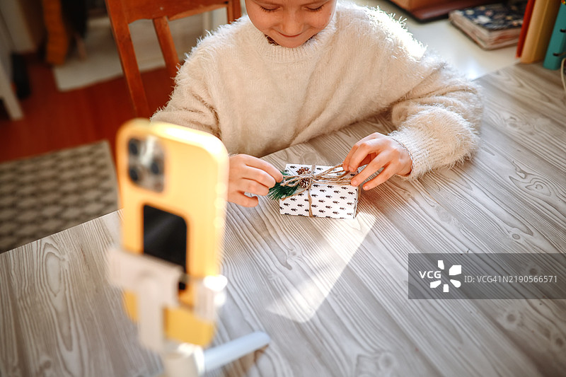 年轻的内容创作者在家拍摄一段引人入胜的开箱视频，专注于一个惊喜礼物，同时使用三脚架进行拍摄。图片素材